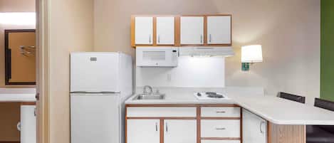A compact kitchen with white appliances, wooden cabinets, a sink, and a dining area with a table and chairs.