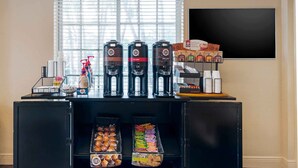Een koffiehoek met verschillende koffieautomaatjes, een assortiment gebak en een schoolbord met een menukaart.