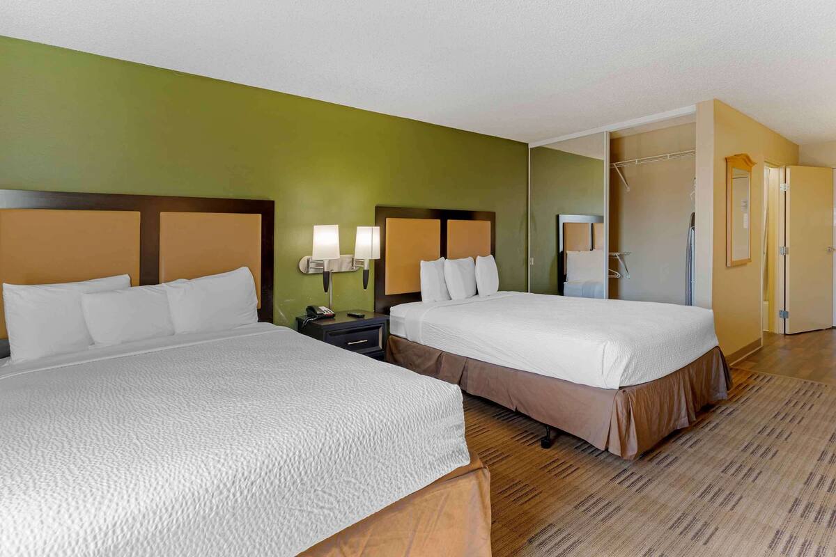 A hotel room with two beds, a nightstand with lamps, a walk-in closet, and a bathroom with a shower and toilet.
