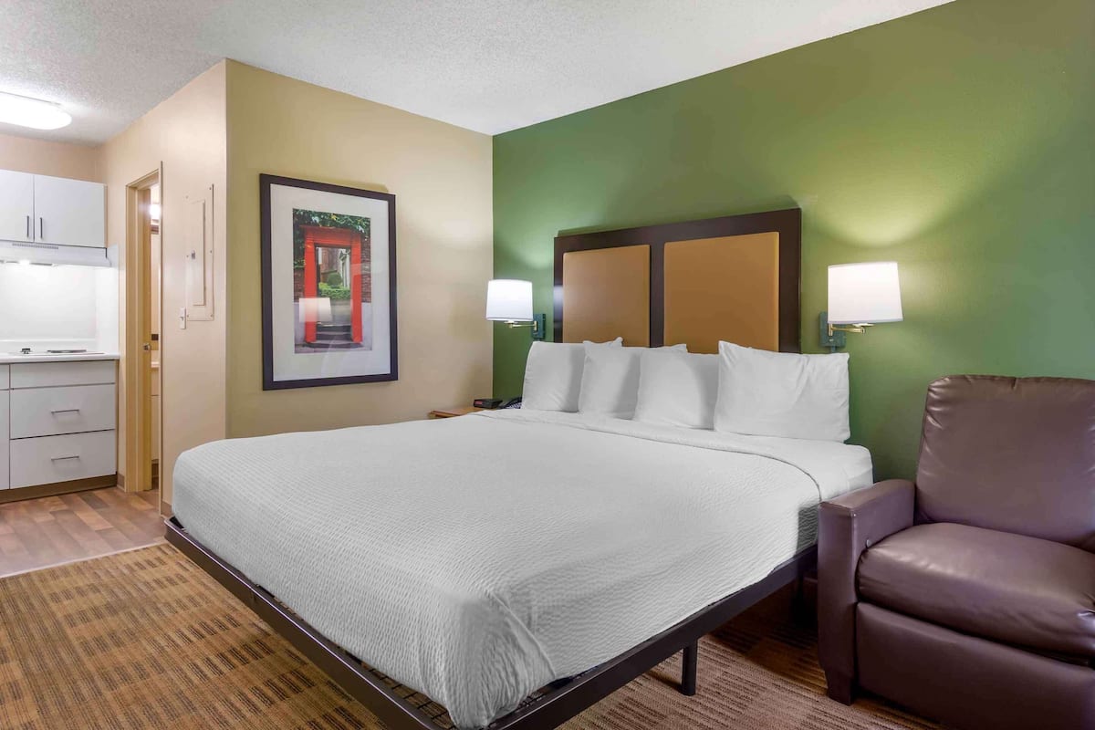 A hotel room with a large bed, a brown leather chair, a small desk, and a framed picture on the wall.
