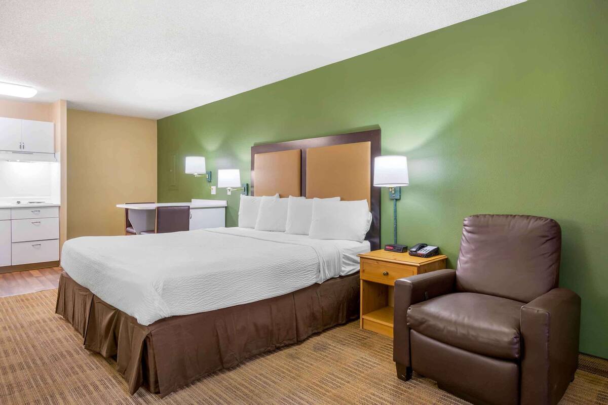 A hotel room with a large bed, bedside tables, a chair, and a small desk.