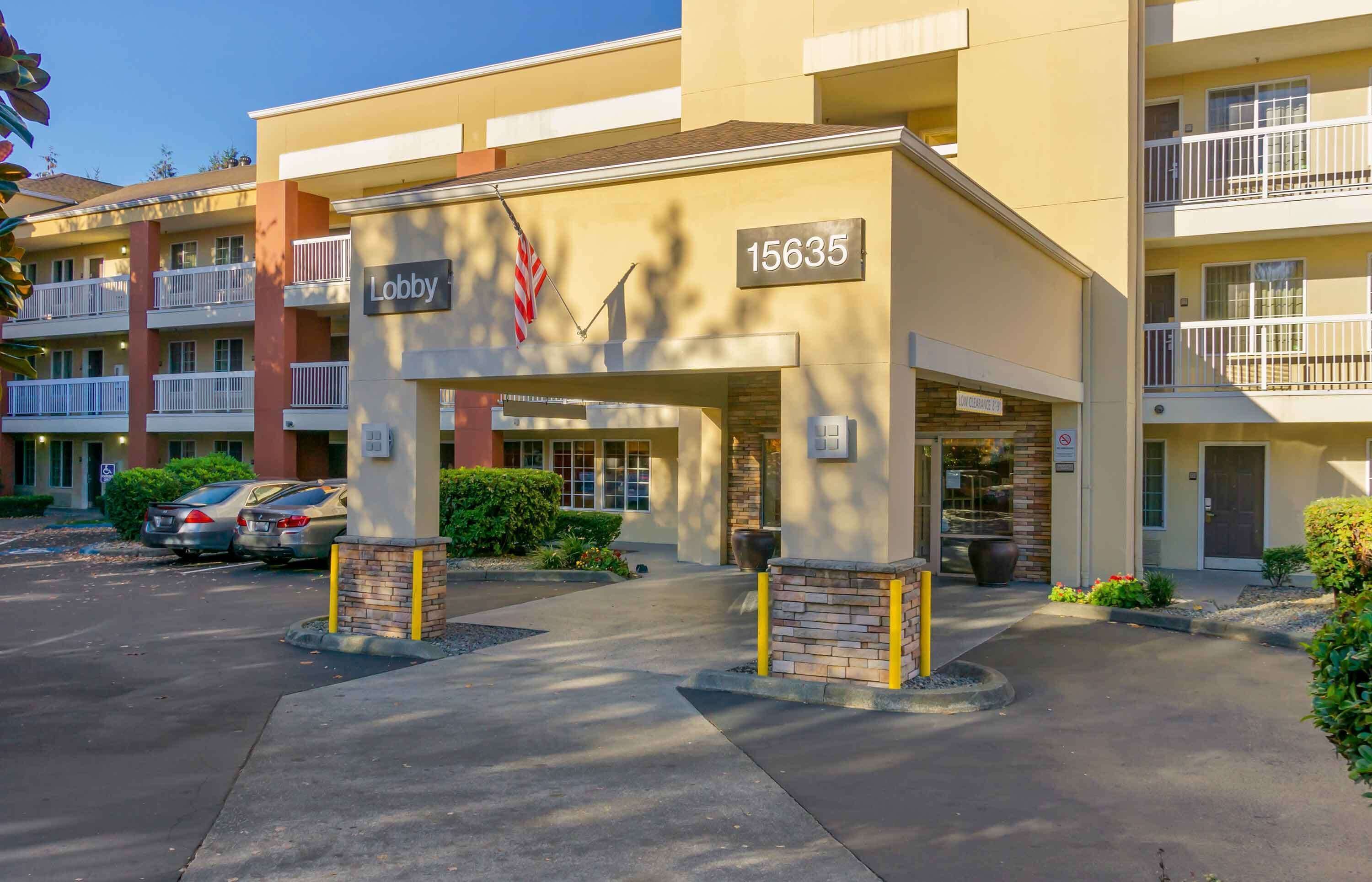 Entrada de hotel com uma placa indicando "Lobby" e o número 15635. Há carros estacionados na frente, e o edifício possui várias sacadas.
