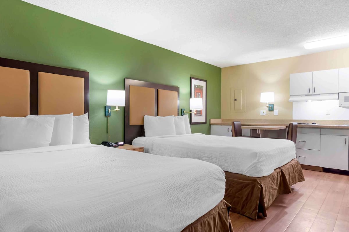 A hotel room with two beds, a kitchenette, and a green wall.