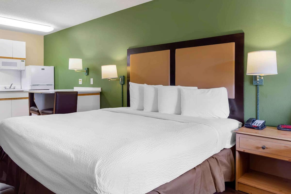 A hotel room with a large bed, a desk with a chair, a microwave, and two wall-mounted lamps.