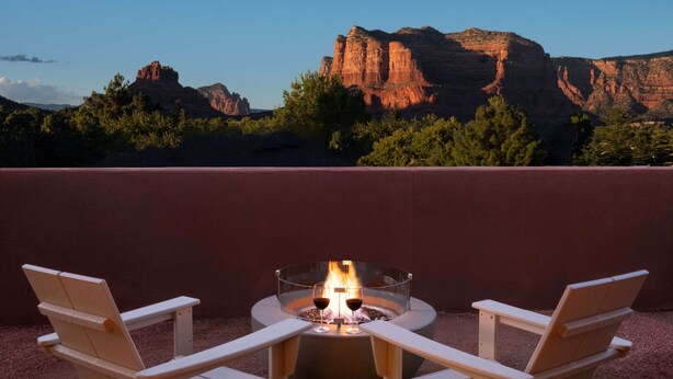 A fire pit with two glasses of wine, surrounded by Adirondack chairs, set against a backdrop of red rock formations and trees. - Hilton Sedona Resort at Bell Rock (Sedona)