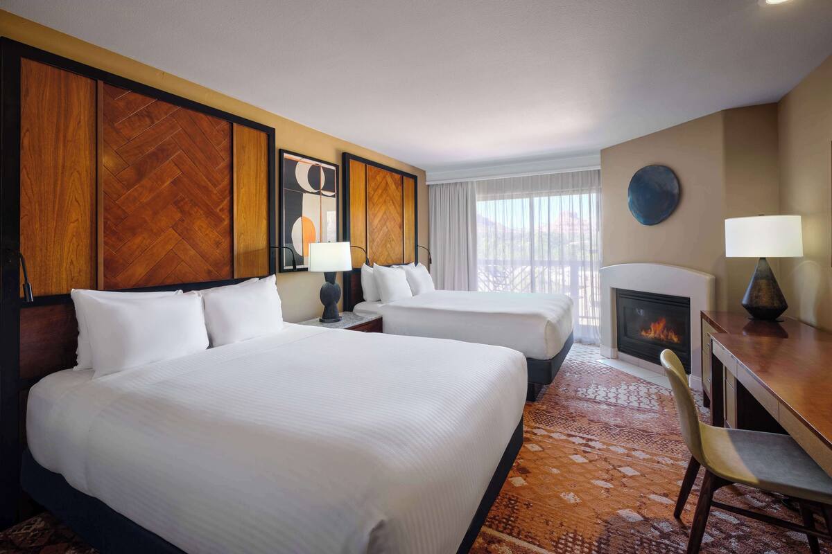 A hotel room with two beds, a fireplace, a dining table, and a view of the outdoors.