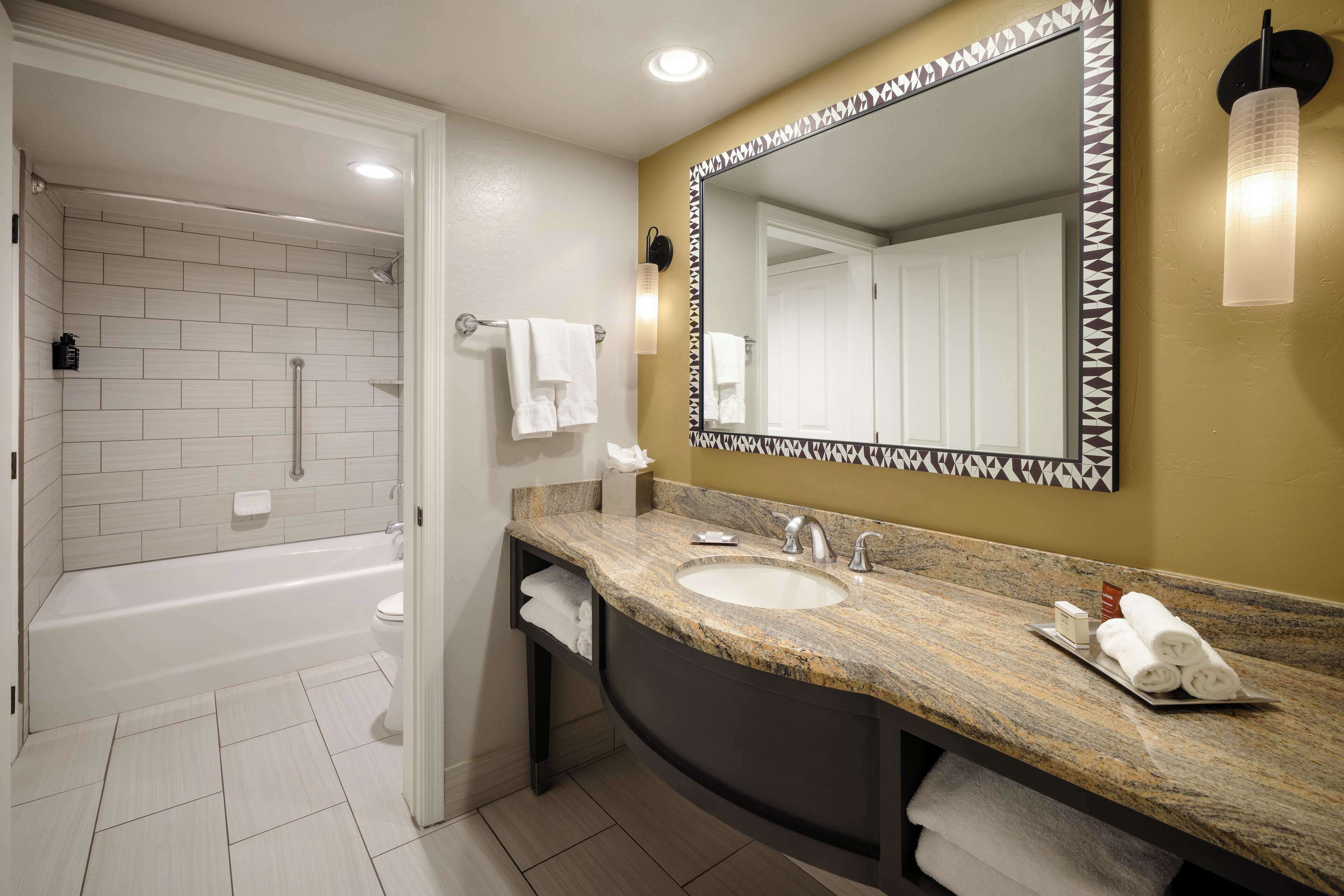 Un baño moderno con bañera, un lavabo grande y un espejo con marco geométrico.