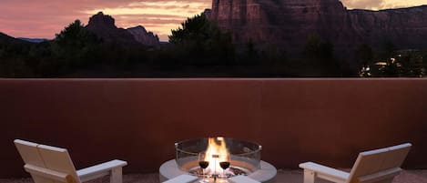 A patio with a fire pit and two chairs facing a mountainous landscape.