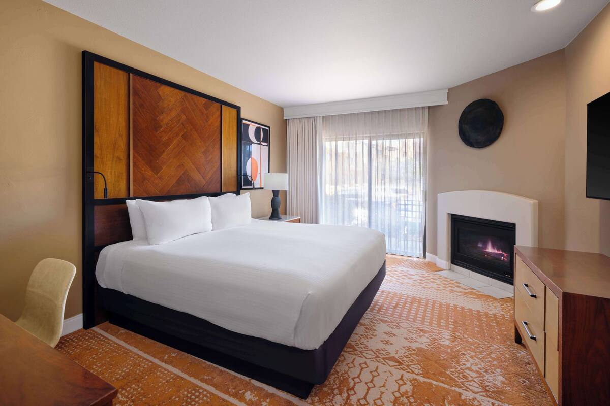 A hotel room with a large bed, a fireplace, a desk, and a chair.