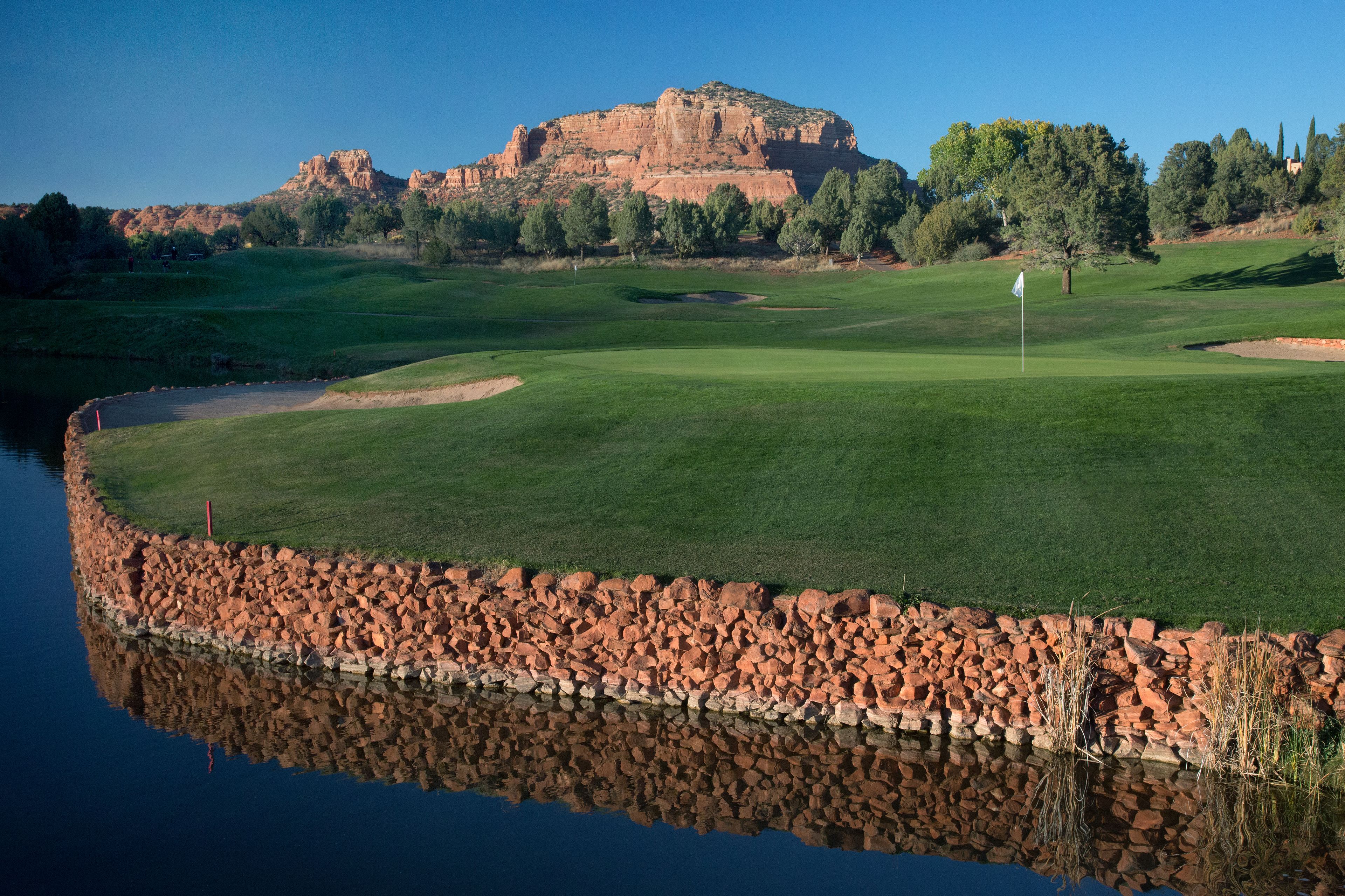 A golf course with a rocky shoreline and a mountain in the background.