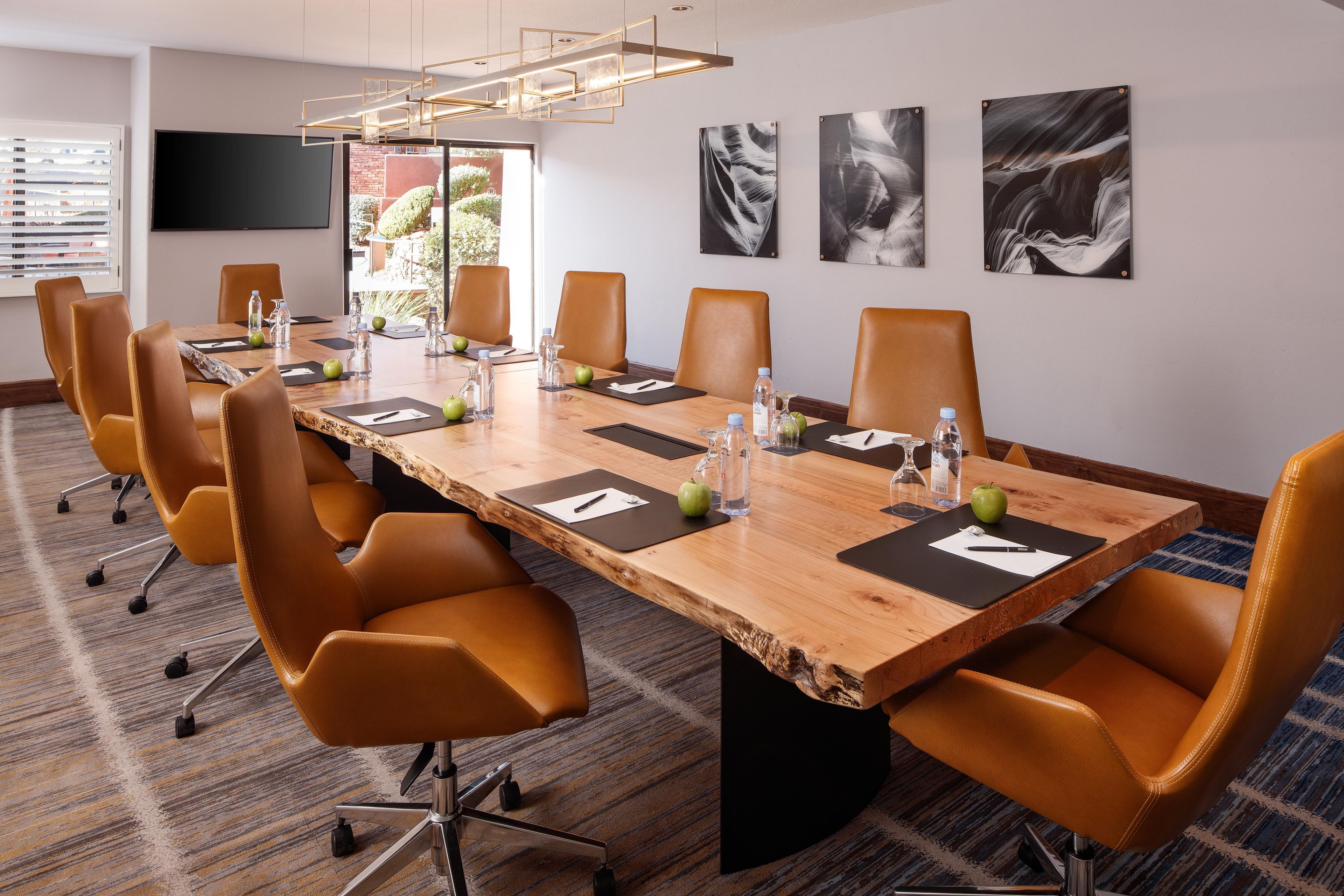 A conference room with a long table, multiple chairs, water bottles, apples, and a television on the wall.