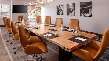 A conference room with a long table, multiple chairs, water bottles, apples, and a television on the wall.