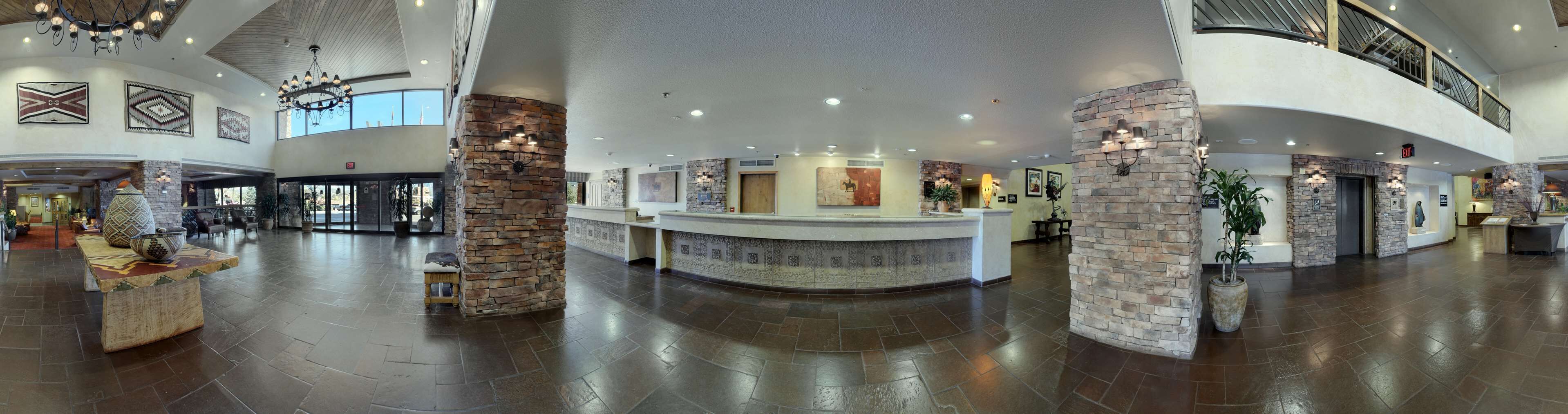 A spacious lobby with a reception desk, stone pillars, and a high ceiling with chandeliers.
