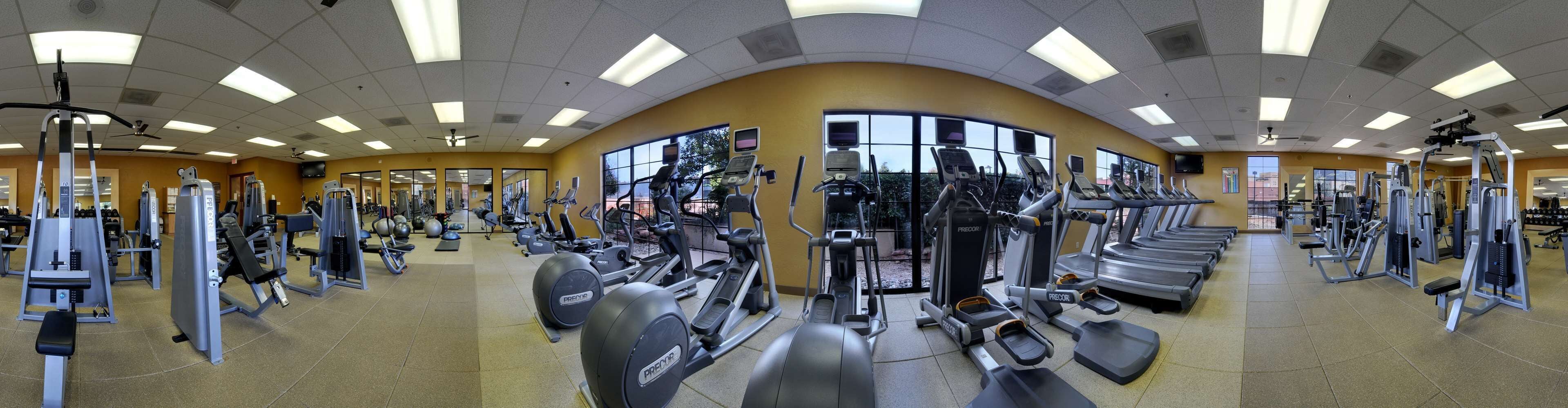 Un gimnasio con diversos equipos de ejercicio, ventanas amplias y un techo curvo.