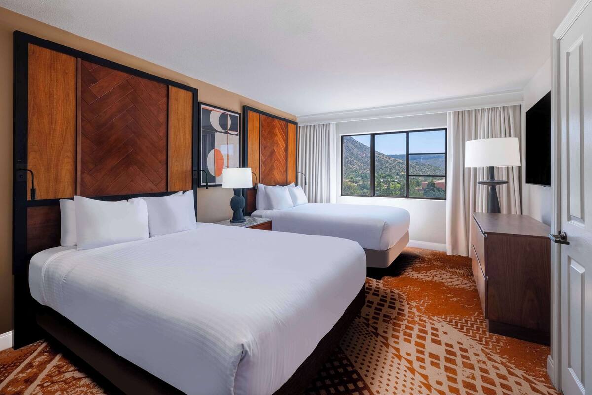 A hotel room with two beds, a TV, a desk, and a view of the mountains.