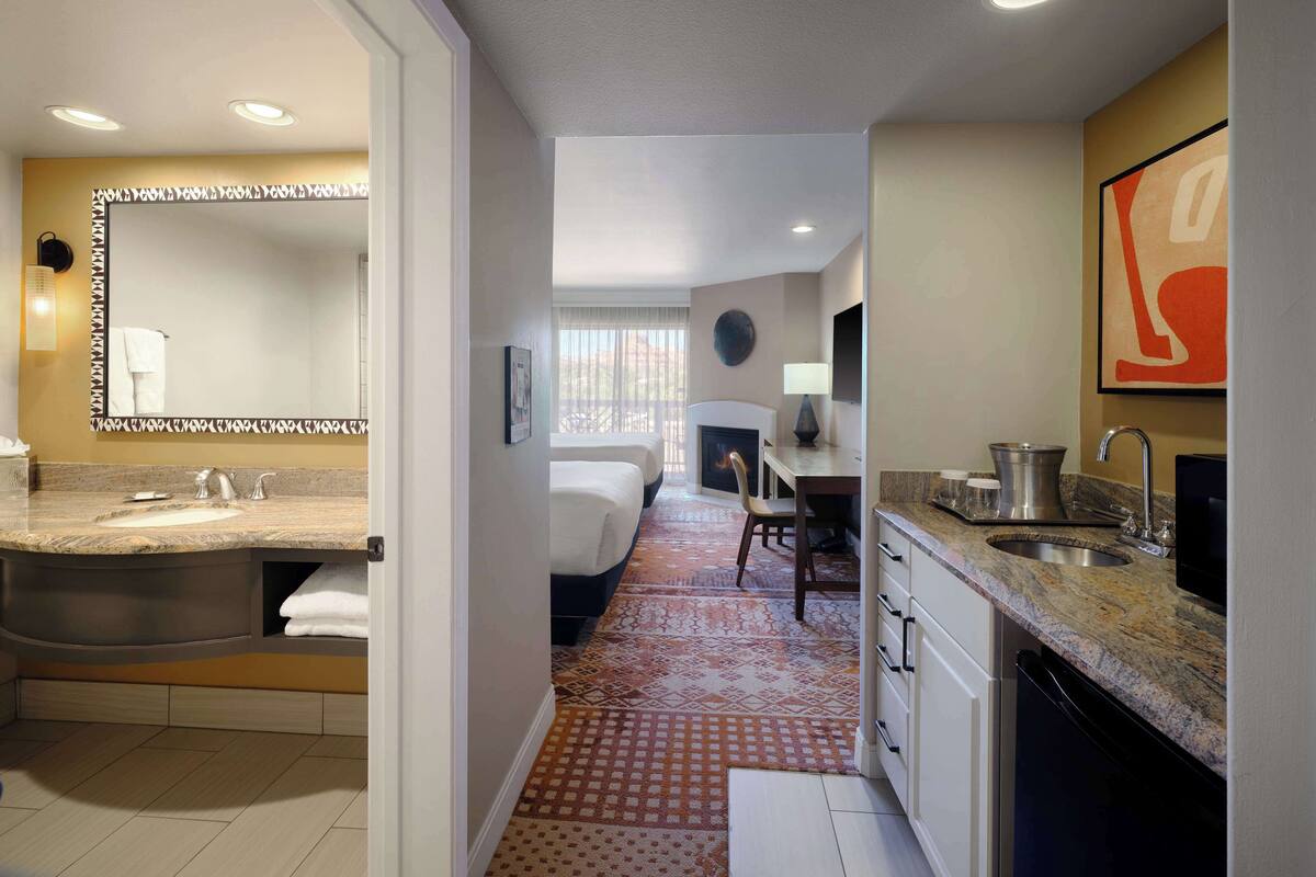 A modern hotel room with a bathroom, kitchenette, and a dining area.