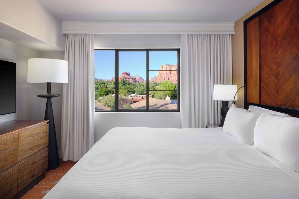 A hotel room with a large bed, two bedside lamps, a wooden dresser, and a TV.
