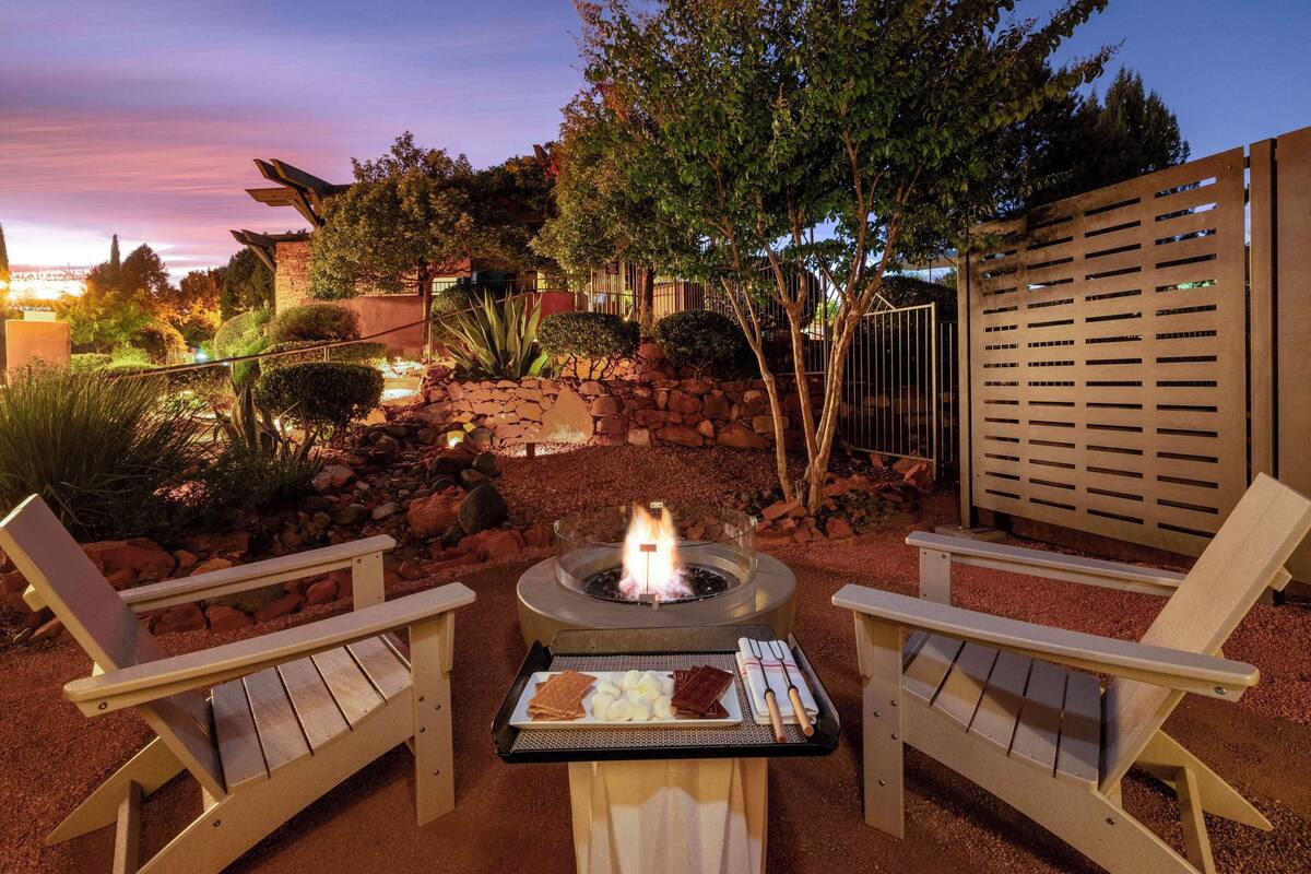An outdoor seating area with Adirondack chairs, a fire pit, and a grill with food.