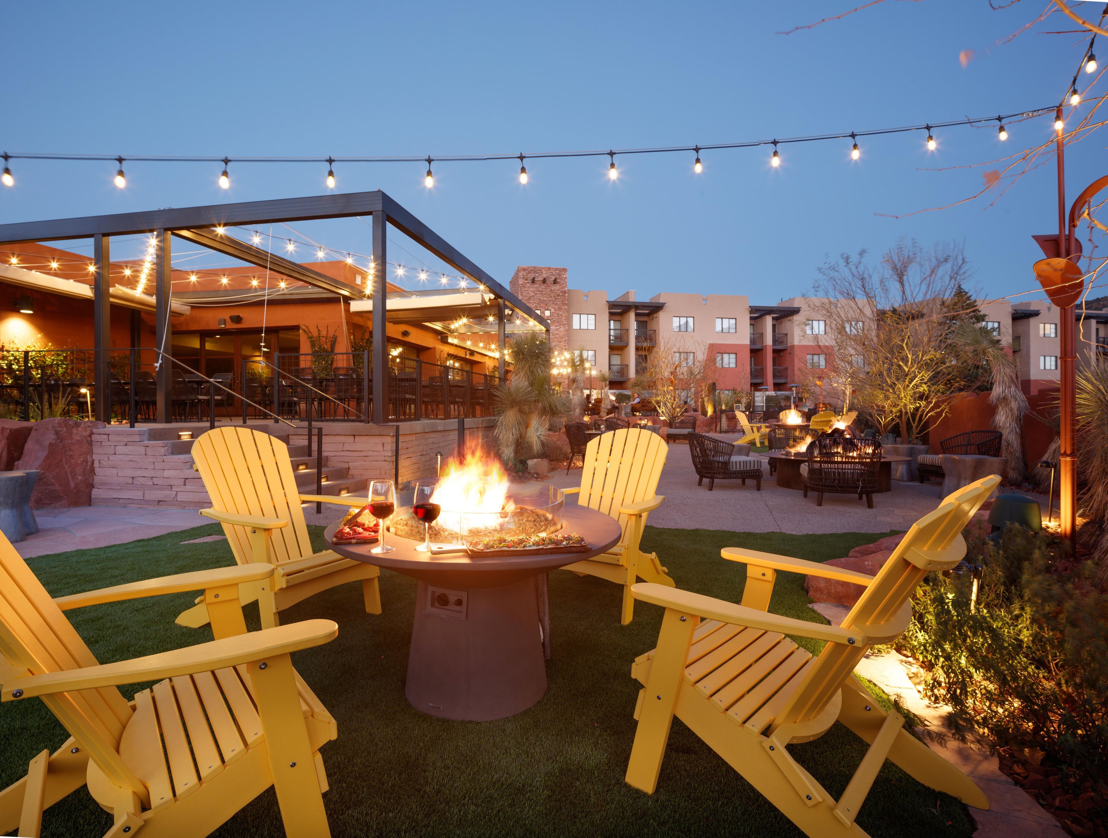 An outdoor patio area with yellow Adirondack chairs, a fire pit, and string lights.