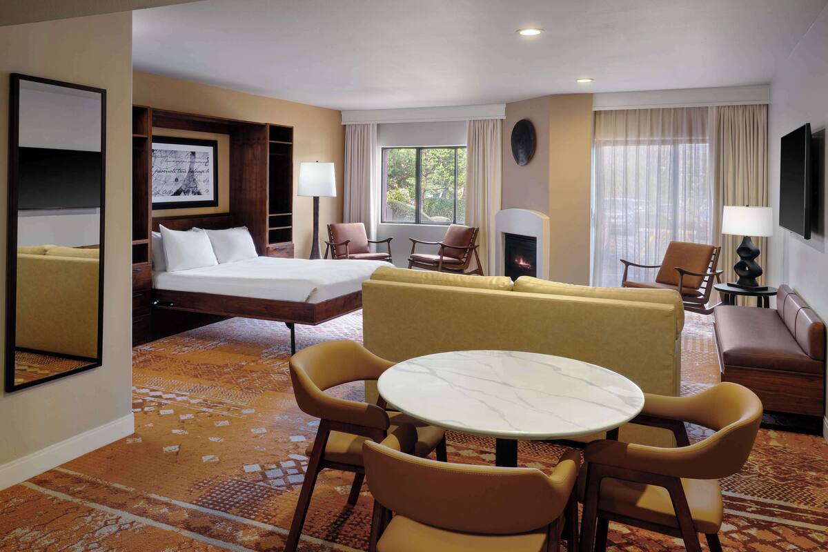 A hotel room with a bed, sofa, armchair, table, and fireplace.