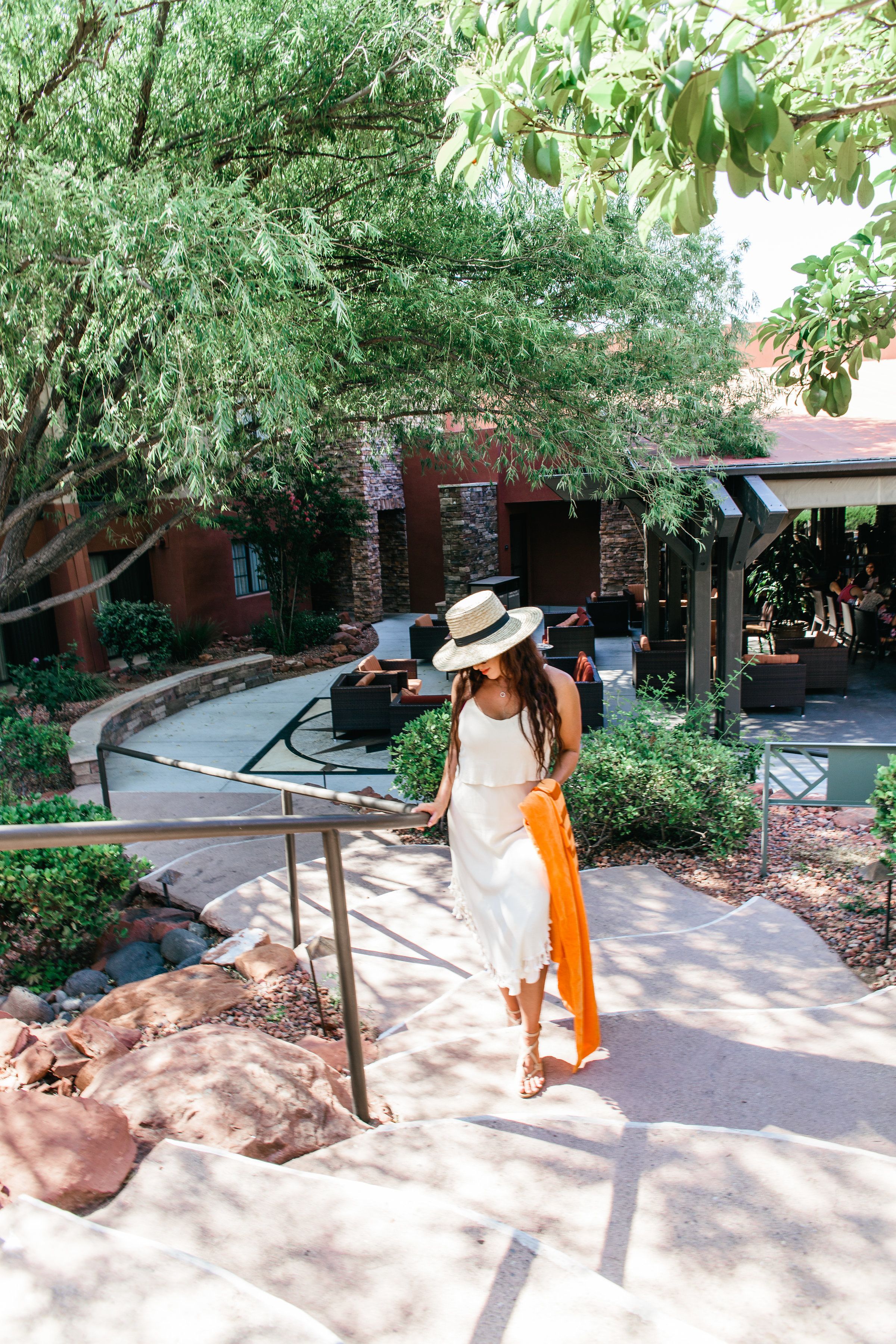 A woman descending a stone staircase in a courtyard with outdoor seating and greenery.