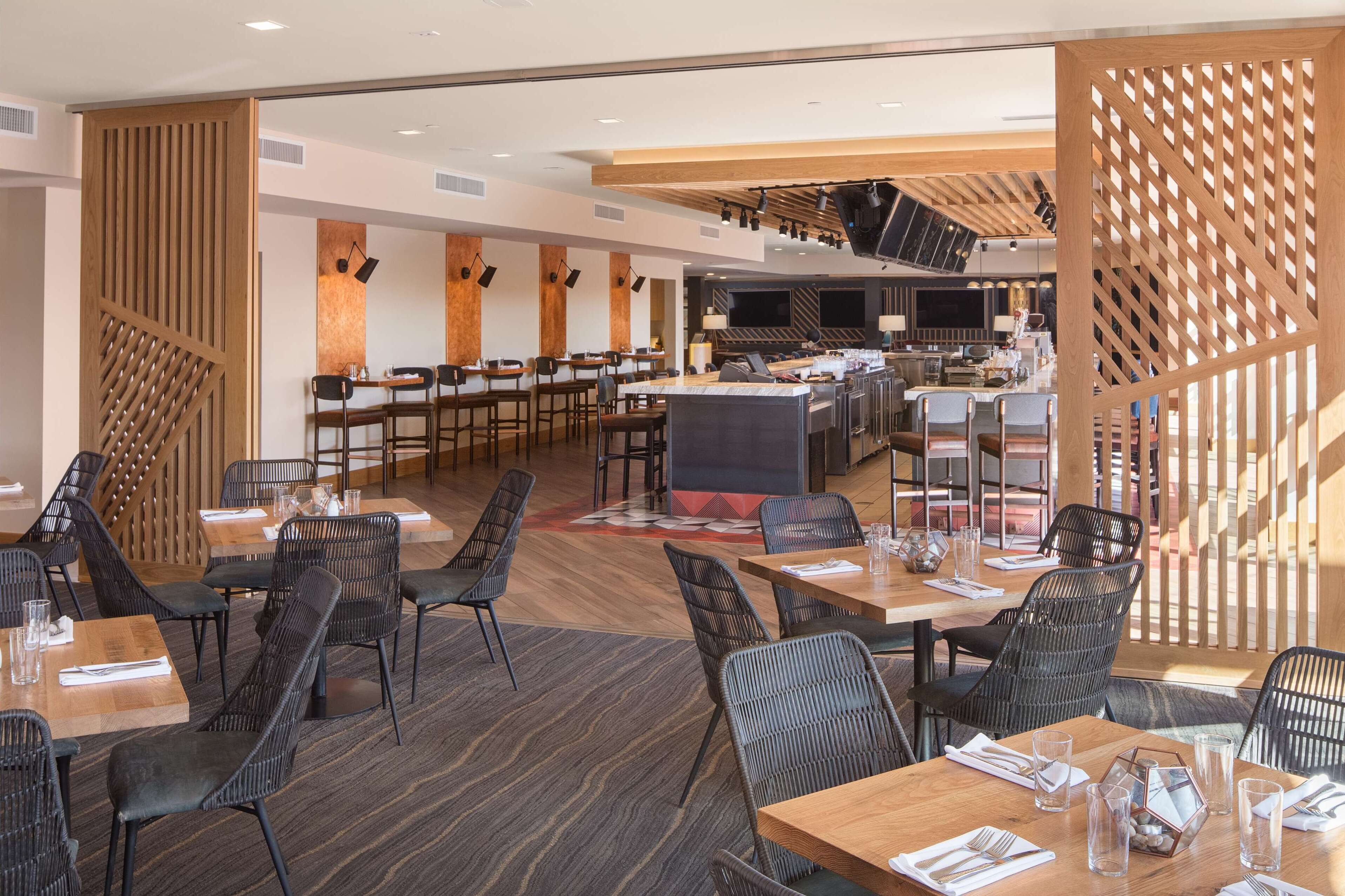 A modern restaurant with wooden accents, black chairs, and a central bar area.