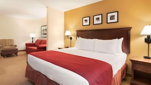 A hotel room with a large bed, two bedside tables with lamps, a red sofa, a striped armchair, and a small table with a lamp.