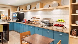 A modern kitchen with blue cabinets, a coffee machine, a buffet station, and a seating area with a wooden table and chairs.