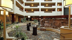 A multi-level hotel lobby with a central courtyard, featuring a patterned floor, multiple levels of balconies, and a rock formation.