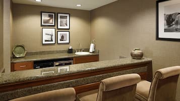 A hotel bathroom with a granite countertop, sink, and two chairs. There are framed pictures on the wall and a vase on the countertop.