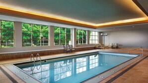 An indoor swimming pool with clear windows, chairs, and a tiled floor.