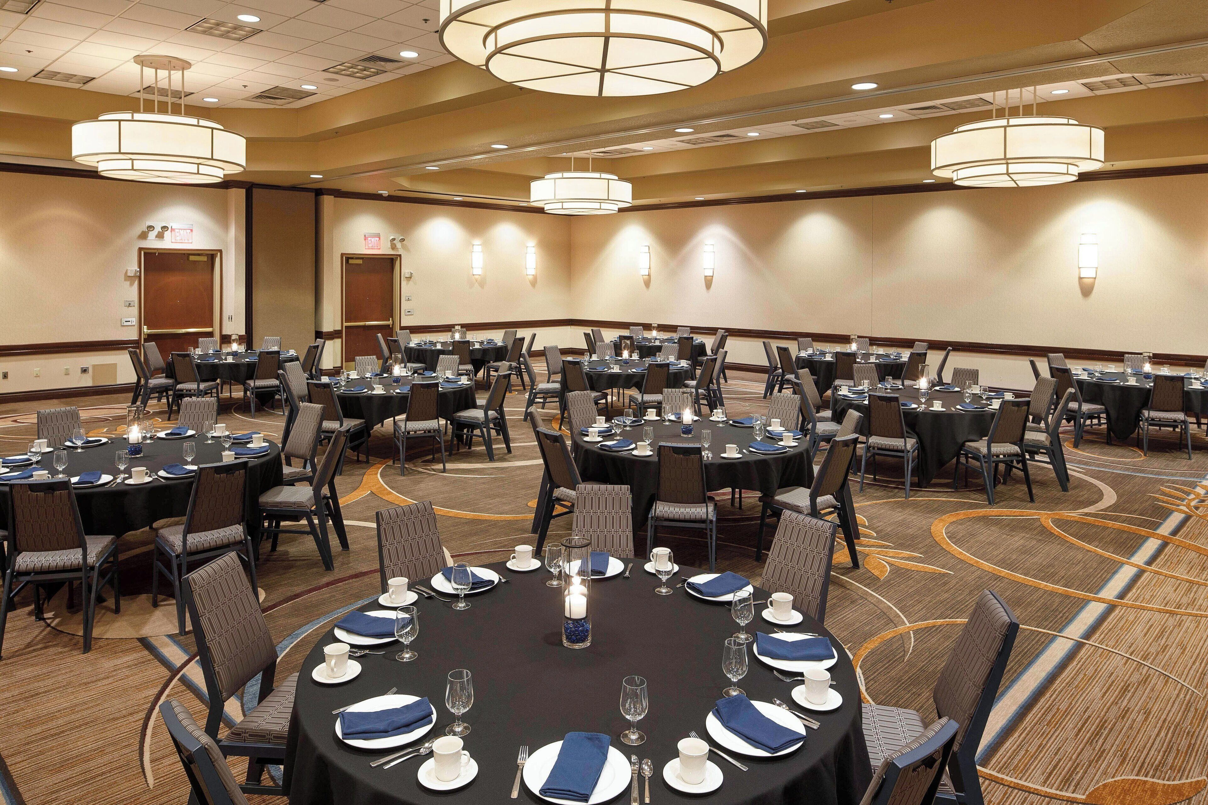 A conference room with multiple round tables, each set with plates, glasses, and chairs.