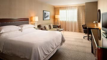 A hotel room with a large bed, a desk with a television, a chair, and a sofa.