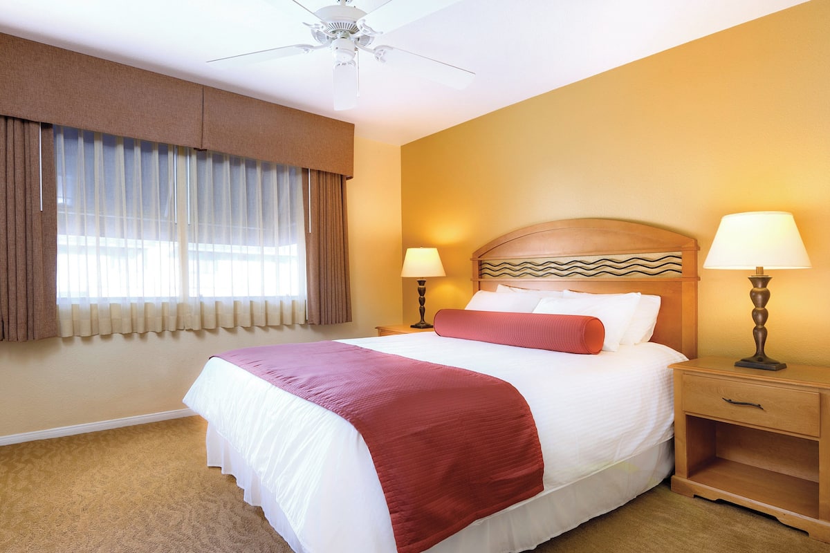 A hotel room with a large bed, two bedside lamps, a wooden nightstand, and a ceiling fan.