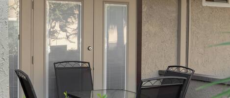 A patio with a glass table and chairs, a door with a window, and a wall-mounted light fixture.