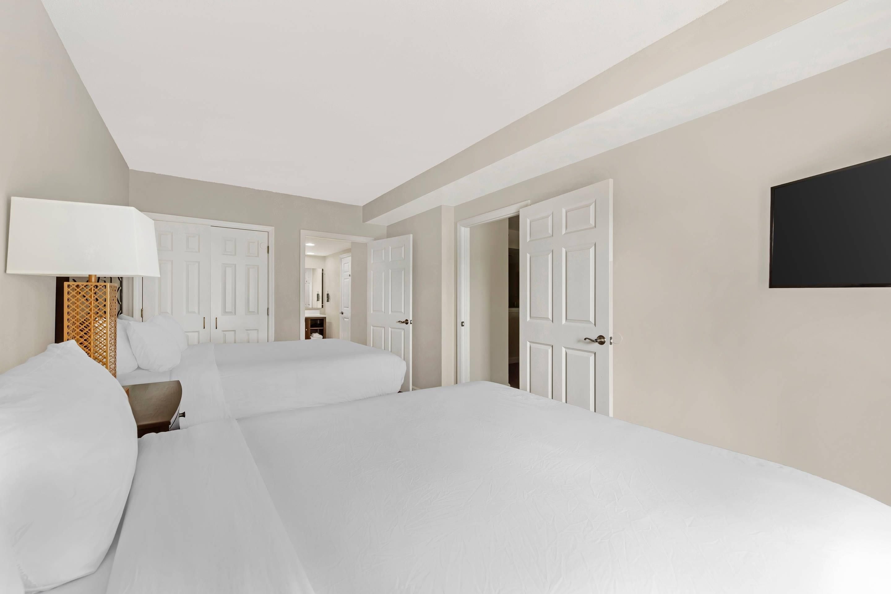 A hotel room with two beds, a bedside table, a lamp, and a wardrobe.