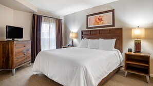 Una habitación de hotel con una cama grande, un televisor sobre una cómoda de madera, una mesita de noche con una lámpara y un cuadro en la pared.