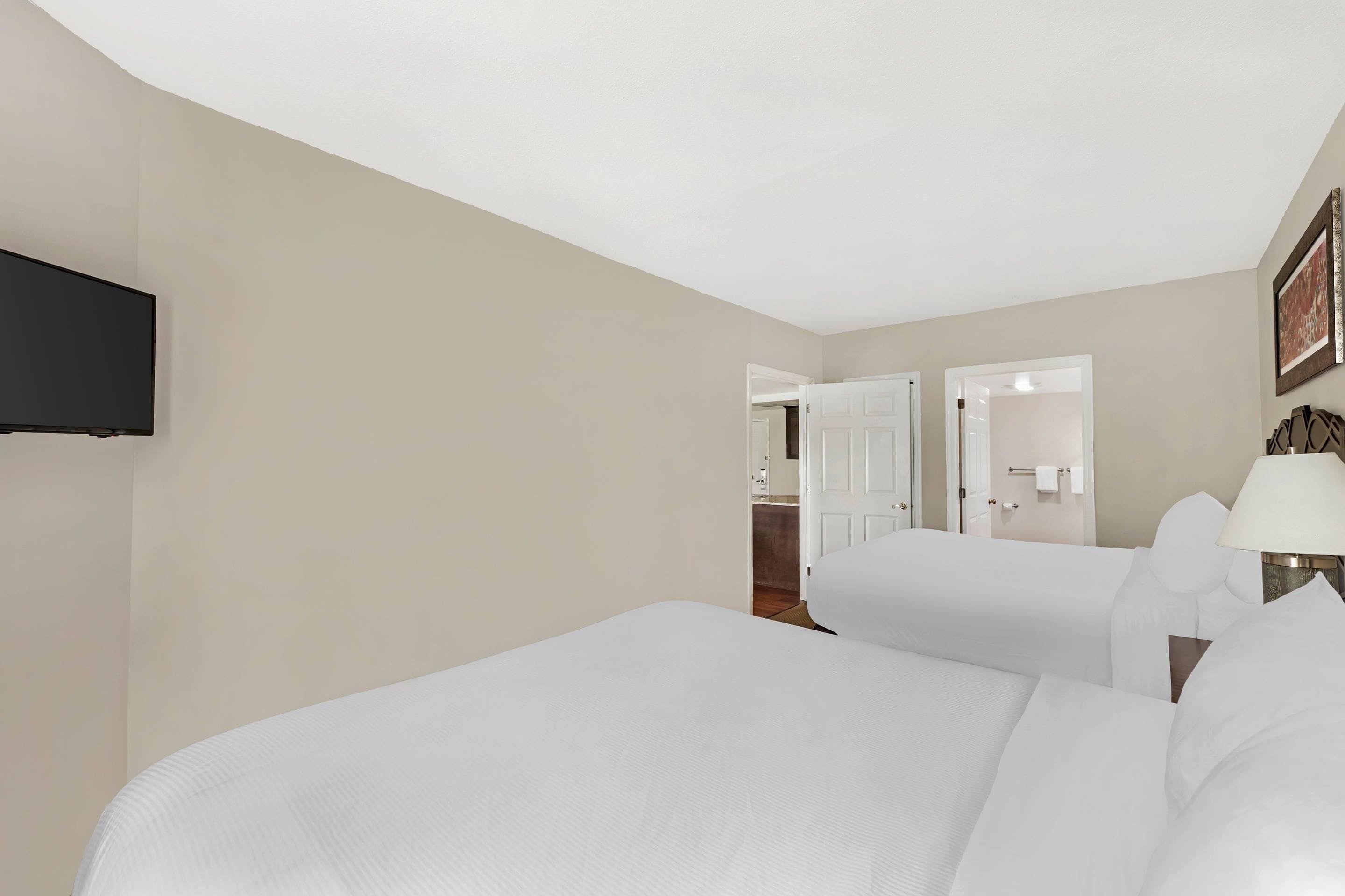 A hotel room with two beds, a television mounted on the wall, and a door leading to a bathroom.