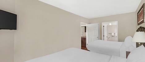 A hotel room with two beds, a television mounted on the wall, and a door leading to a bathroom.
