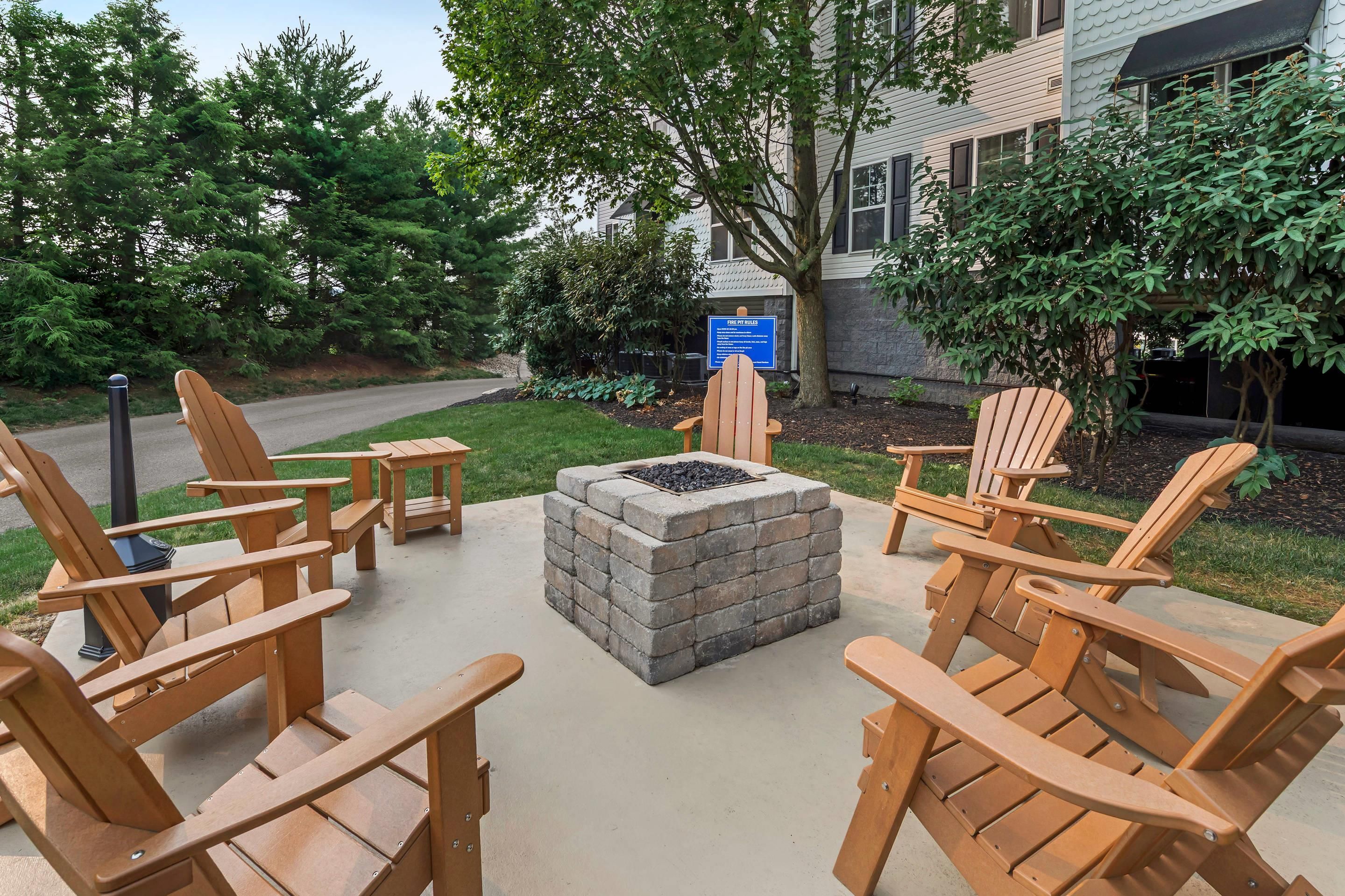 An outdoor seating area with wooden Adirondack chairs and a stone fire pit.