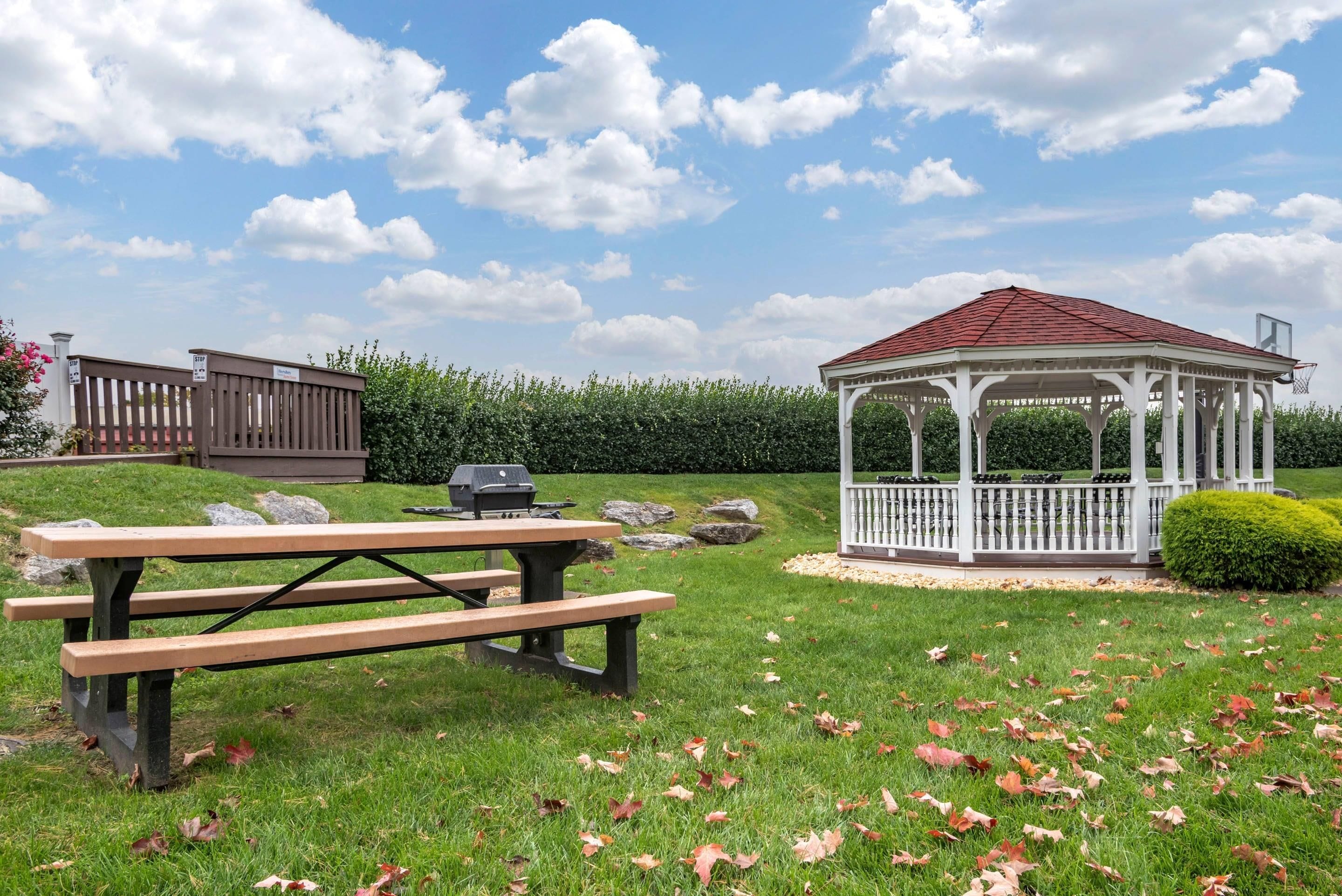 A gazebo with a red roof, a picnic table with benches, and a barbecue grill.