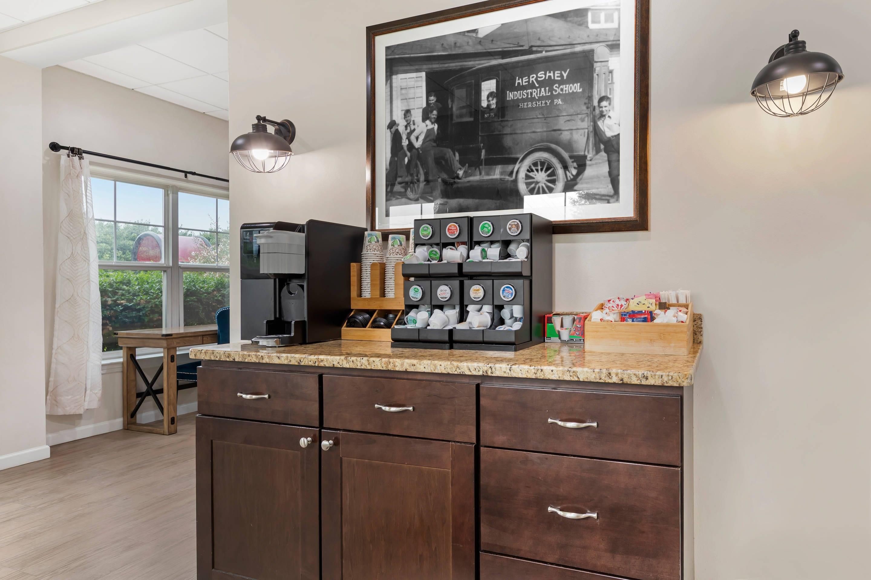A kitchen with a coffee station, a framed historical photo, and a window with curtains.