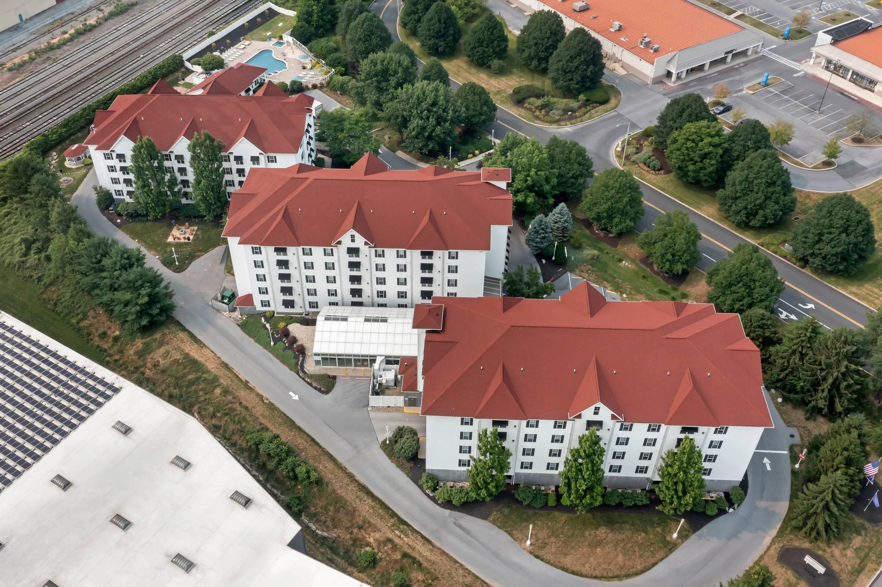 Un hôtel à plusieurs étages, avec un toit rouge, entouré de verdure et doté d’un parking.