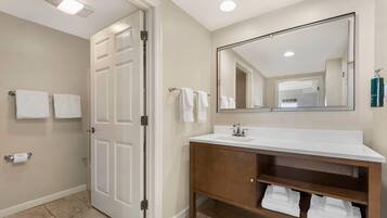 A bathroom with a white vanity, a large mirror, and a door leading to another room.