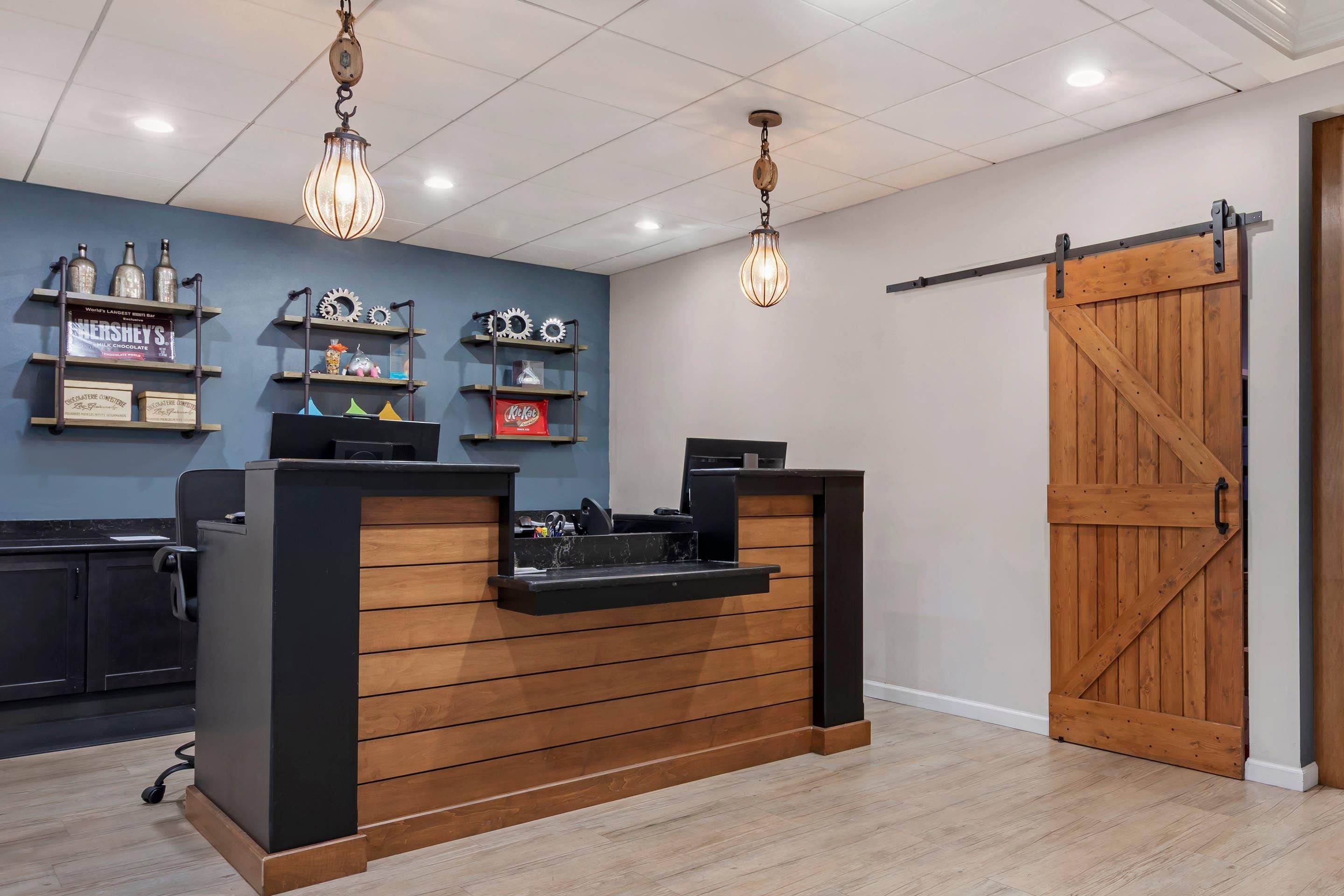 Un mostrador de recepción con detalles de madera, una pared azul con estantes que exhiben diversos objetos y una gran puerta de madera.