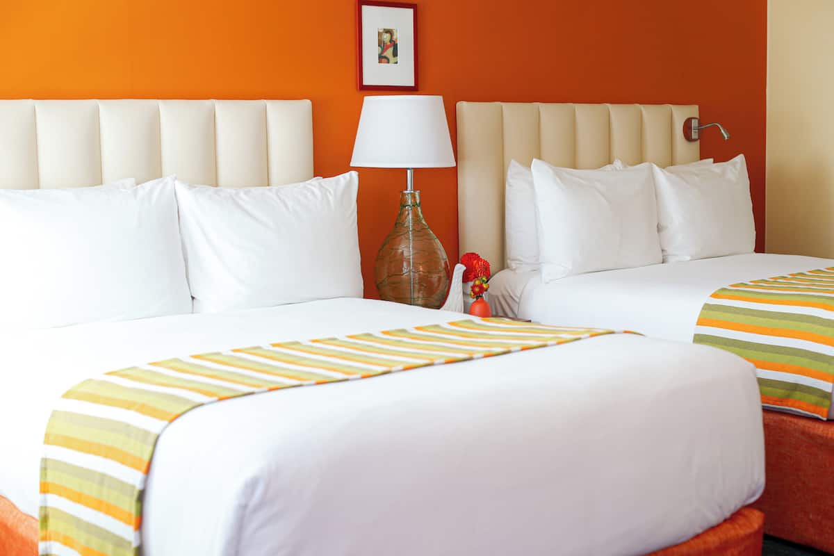 A hotel room with two beds, a lamp, and a framed picture on the wall.