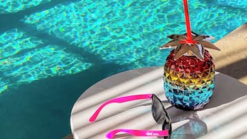 A colorful drink with a straw and sunglasses on a table by a pool.