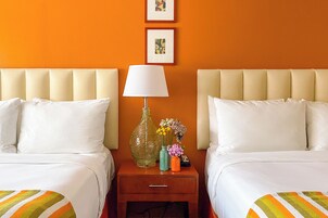 A hotel room with two beds, a nightstand with a lamp, and a vase with flowers.