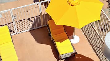 A sunlit outdoor seating area with yellow chairs and an umbrella, enclosed by a white metal fence.