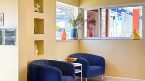 A corner room with two blue armchairs, a small white table, and a window with a view of the outside. - Hotel Del Sol (San Francisco)